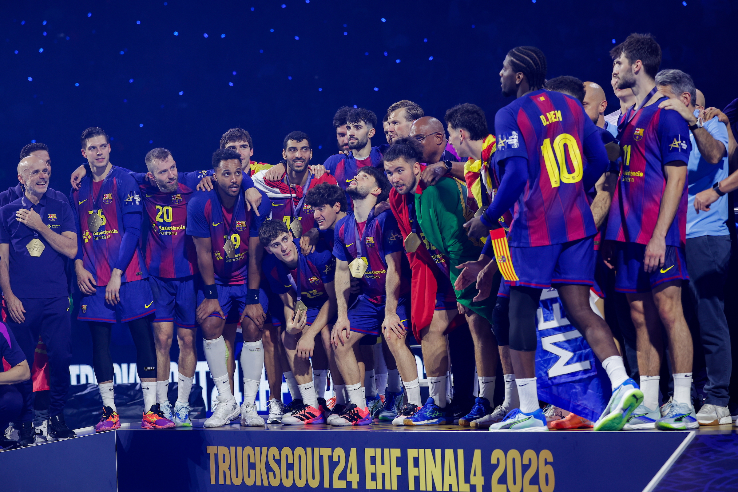 A group of athletes in blue and red jerseys stand together on a podium, celebrating after winning the Truckscout24 EHF FINAL4 2026 tournament.