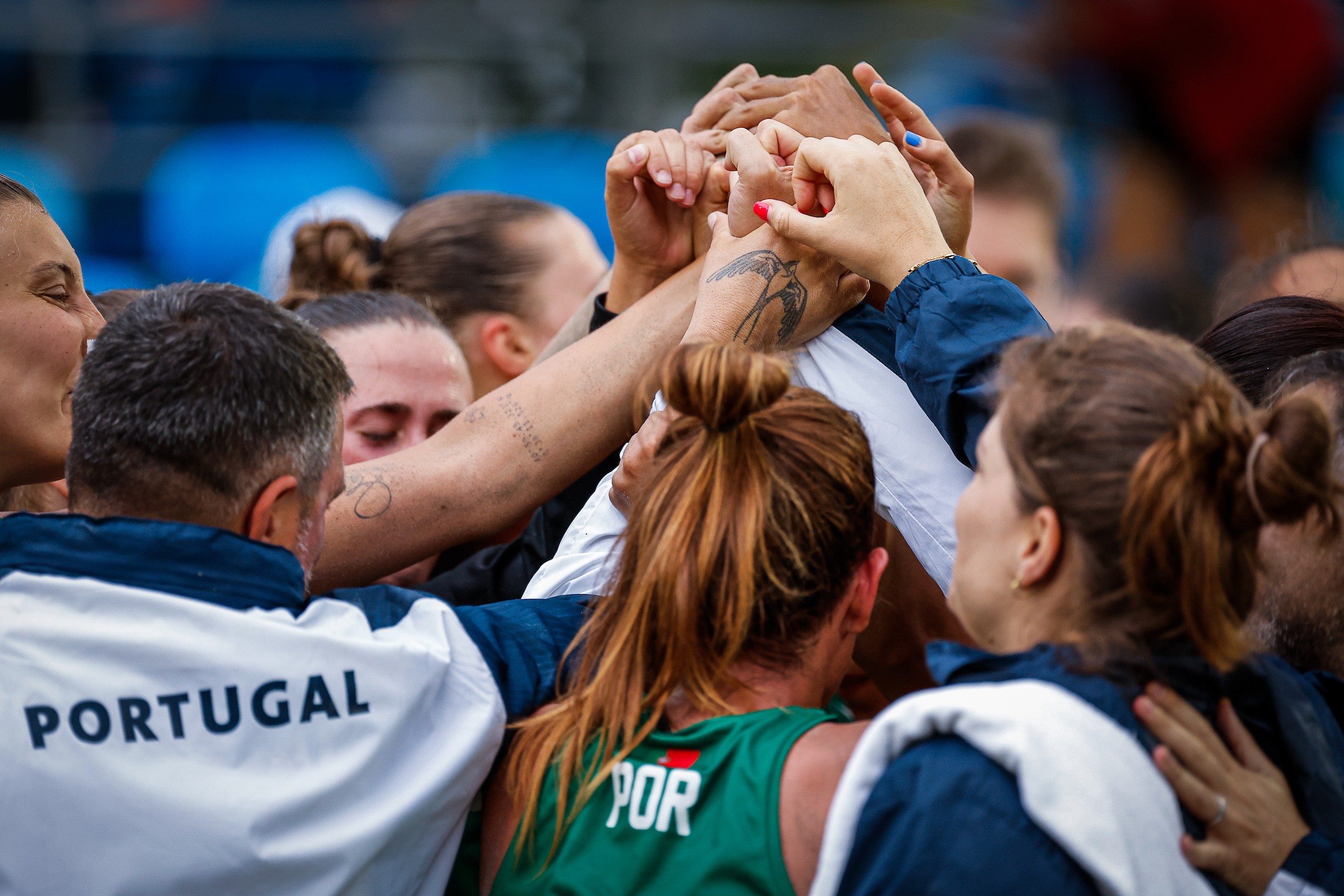 A group of athletes from Portugal gather in a huddle, interlocking hands in a show of unity and teamwork.
