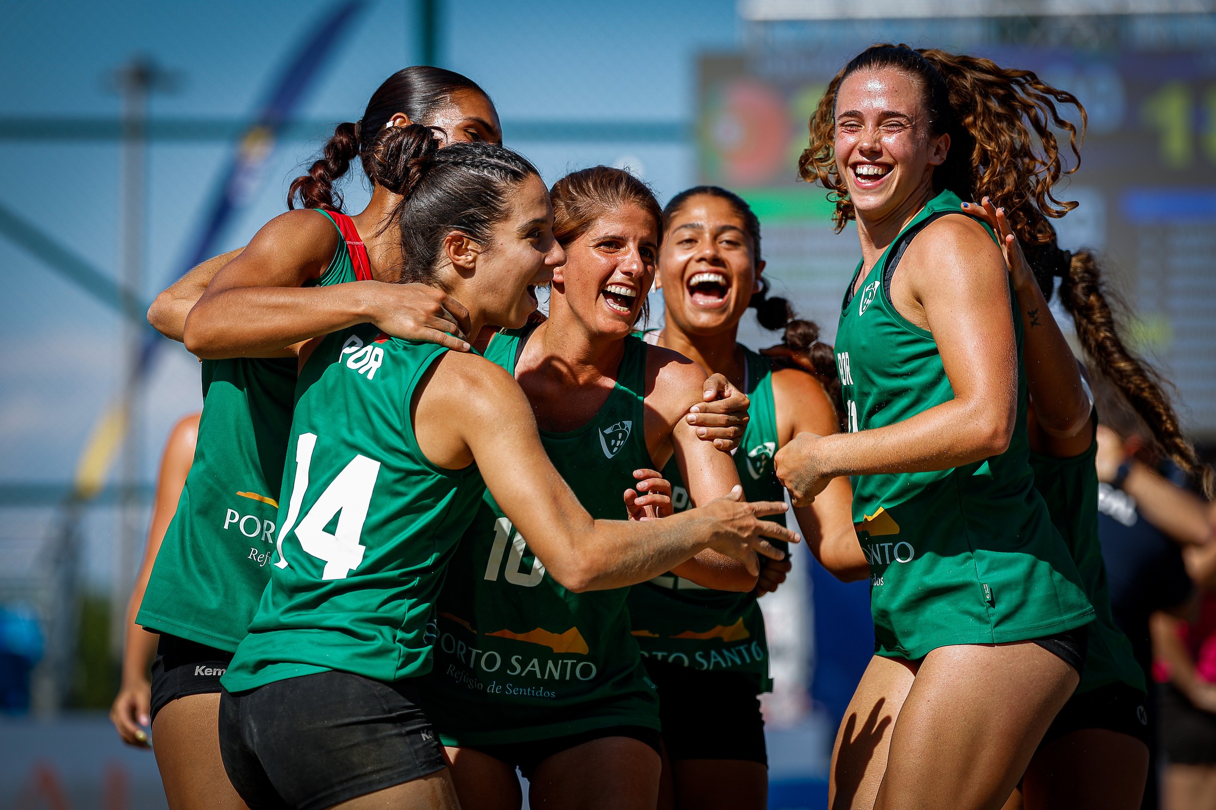 A group of athletes in green jerseys celebrate enthusiastically together on a sports field.