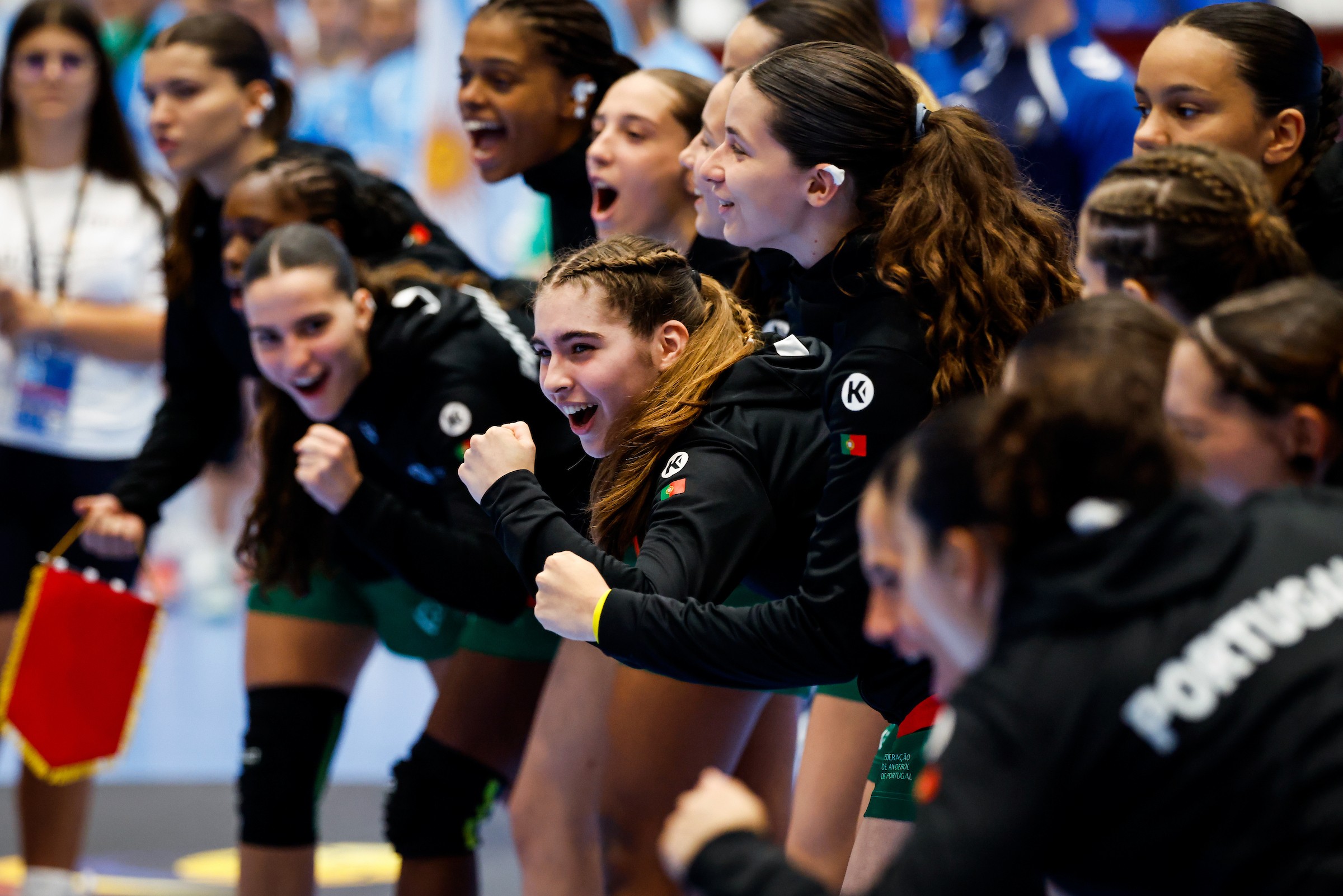 A group of athletes in black jackets with Portuguese flags cheer enthusiastically during a sports event.
