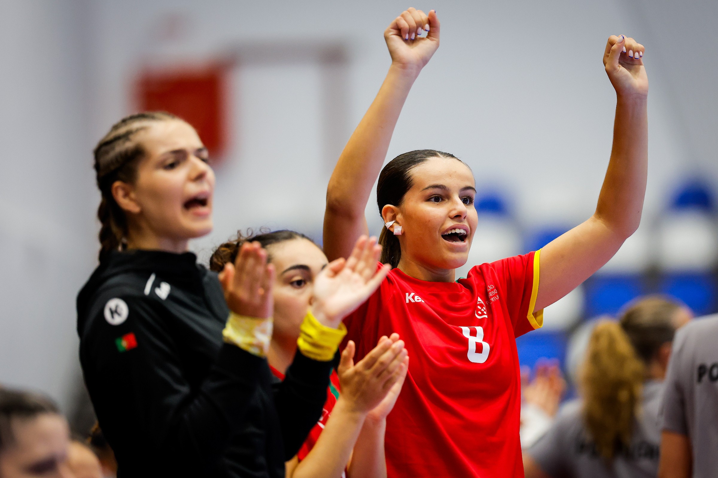Athletes in red and black uniforms celebrate with raised arms and clapping hands during a sports event.