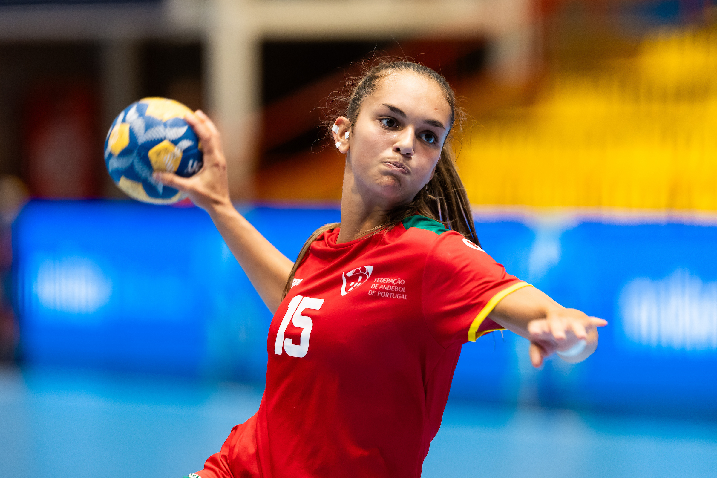 A player in a red jersey with the number 15 prepares to throw a handball during an indoor game.