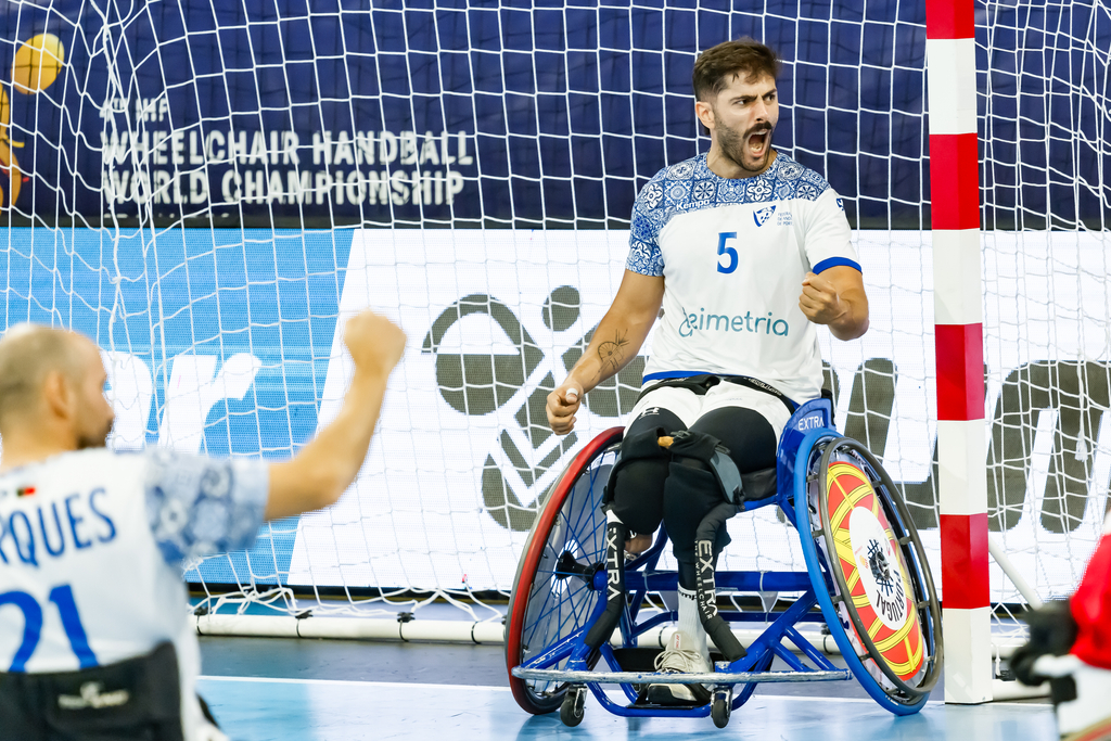An athlete in a wheelchair celebrates with a raised fist during a wheelchair handball match.