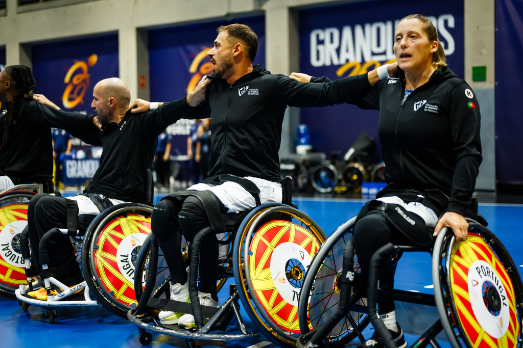 A group of athletes in wheelchairs, wearing matching black jackets and colorful wheel rims, are cheering together during a sports event.