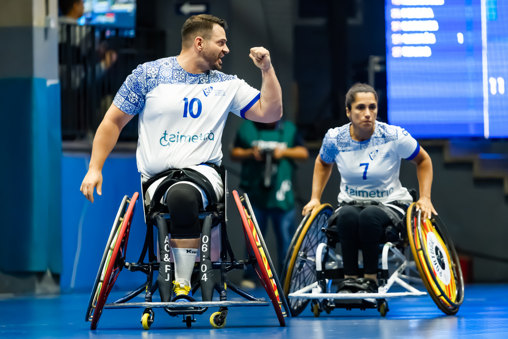 Two athletes in wheelchairs celebrate during a competitive indoor sport, with one raising a fist in triumph.