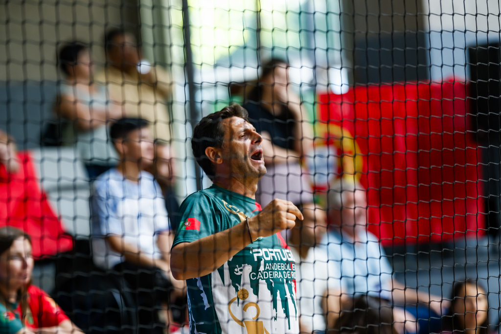 A person in a green and white Portugal-themed shirt reacts with excitement while standing behind a net in a sports arena.