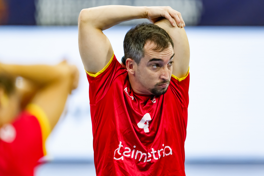 An athlete in a red jersey with the number 4 stretches their arm above their head during a sports event.