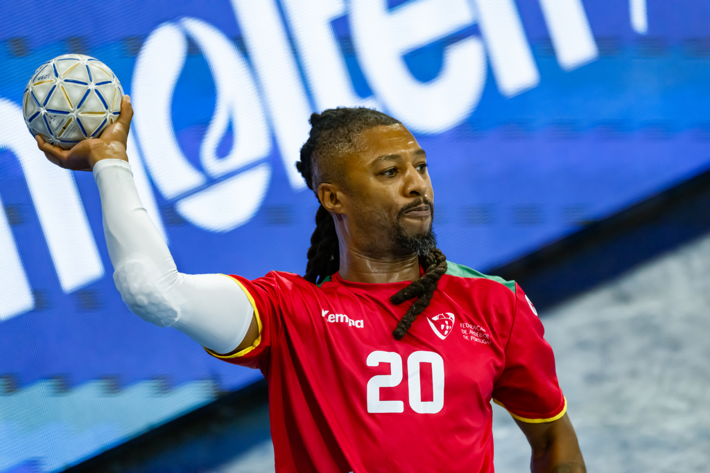 An athlete in a red jersey with the number 20 holds a handball aloft during a game.